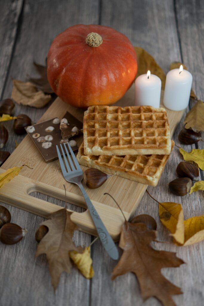 Cozy autumn breakfast scene with waffles, pumpkin, and candles on a wooden table.